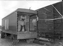 832974 Afbeelding van het overladen van pakketten van trein naar vrachtwagen. De employees dragen petten met de letters ...